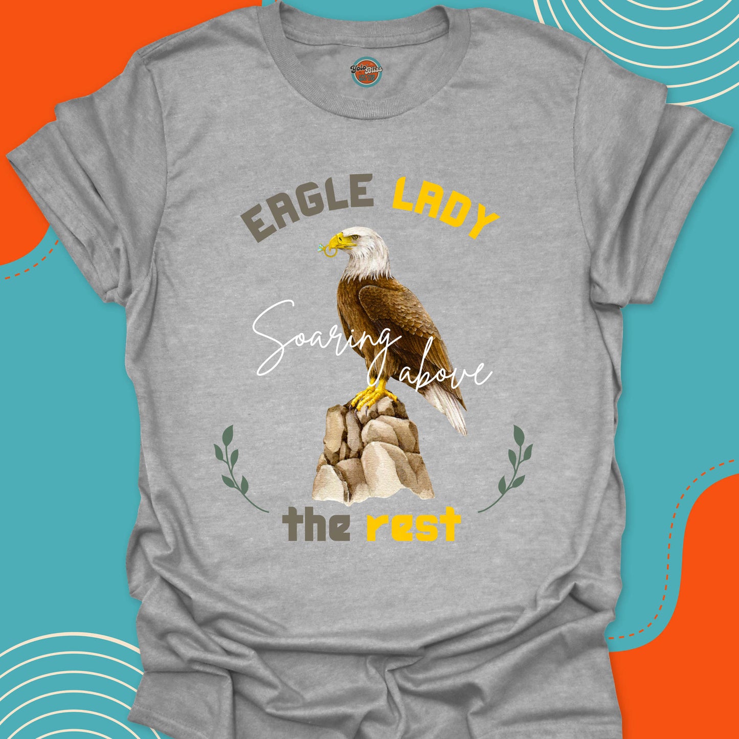 Light gray t-shirt with an eagle on a rocky mountain with a diamond ring in his beak graphic and "Eagle lady, soaring above the rest" text 
