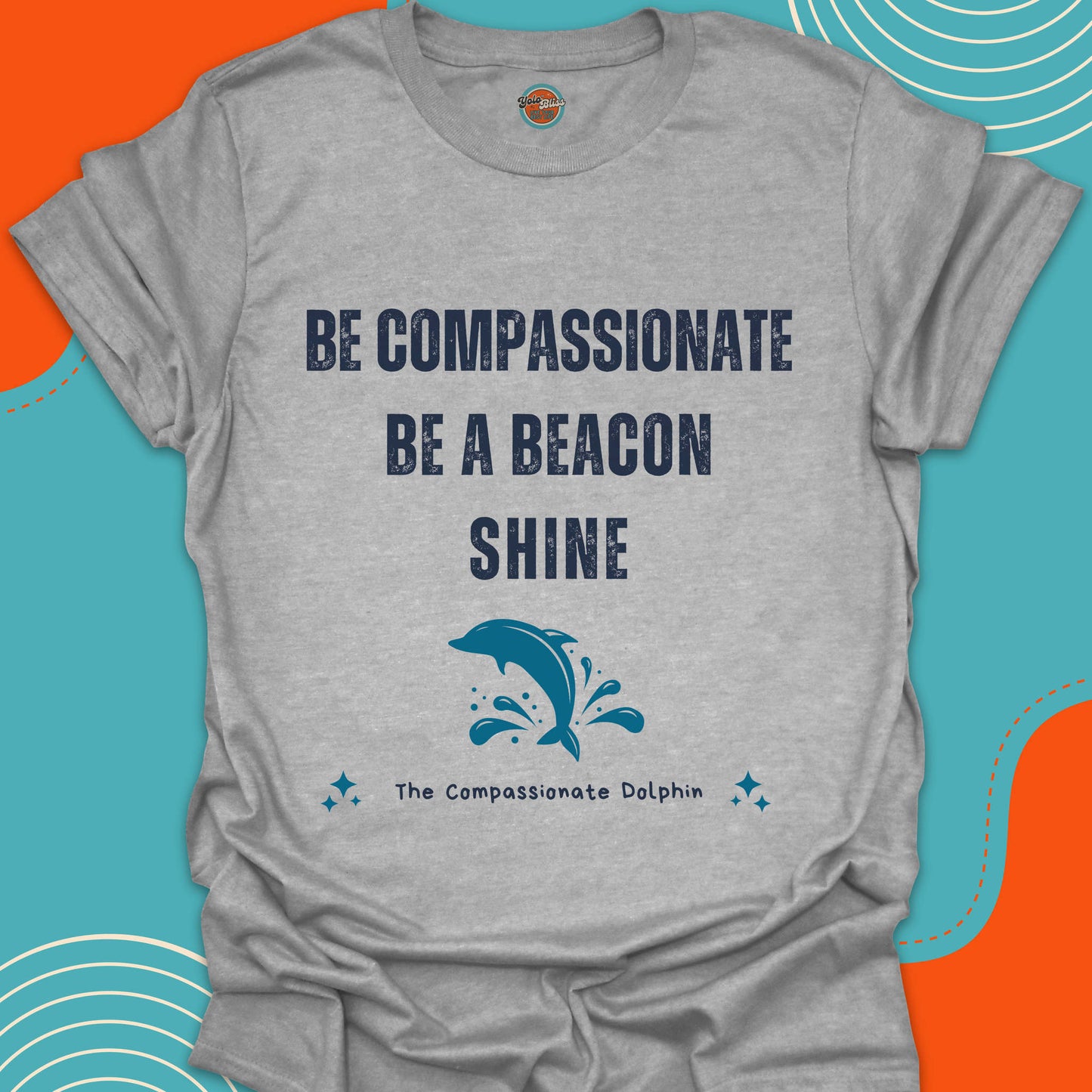 Light gray t-shirt with motivational text "Be compassionate, be a beacon, shine"and jumping blue dolphin in the sea