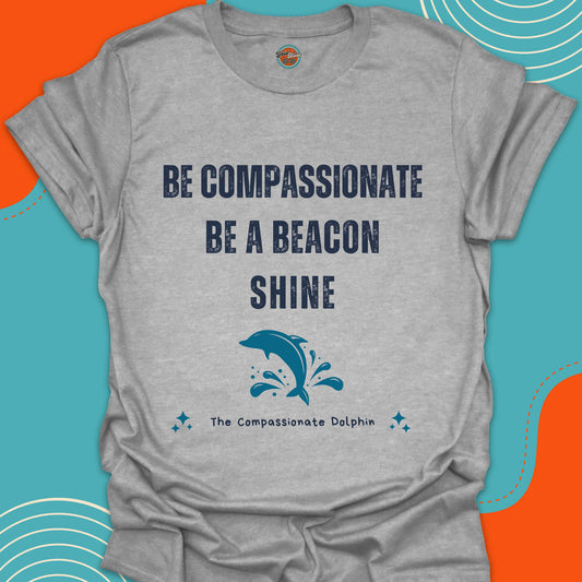 Light gray t-shirt with motivational text "Be compassionate, be a beacon, shine"and jumping blue dolphin in the sea
