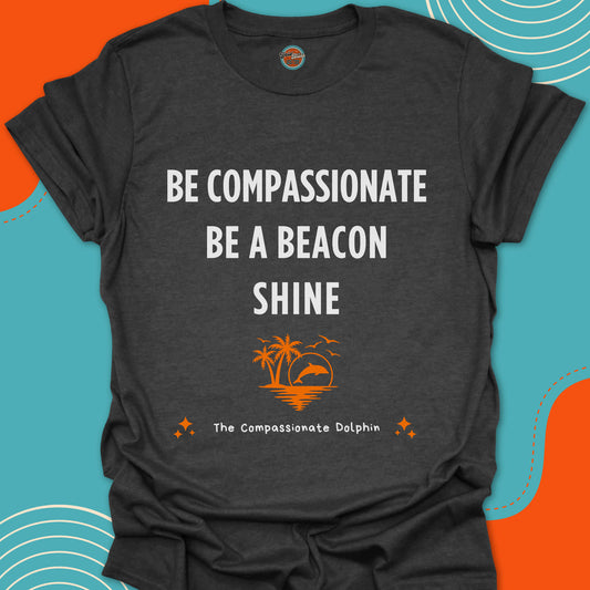 Dark gray t-shirt with motivational quote "Be compassionate, be a beacon, shine"and orange dolphin jumping in the sea graphic.