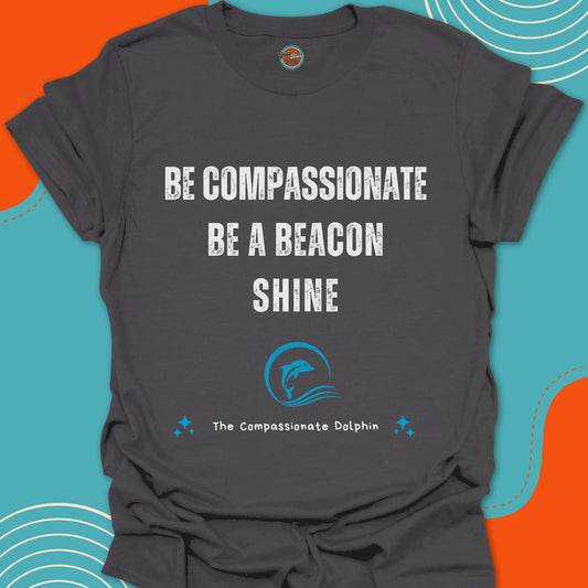 Dark gray charcoal t-shirt with motivational text "Be compassionate, be a beacon, shine"and blue dolphin swimming inside of a wave graphic
