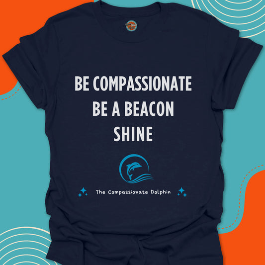 Navy blue t-shirt with white motivational text "Be compassionate, be a beacon, shine"and blue dolphin swimming inside of a wave graphic
