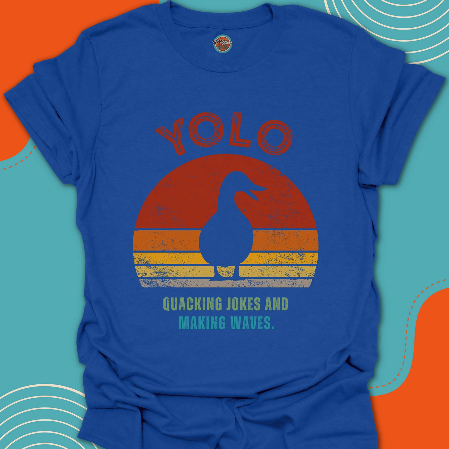 Blue t-shirt with a duck graphic design and 'YOLO Quacking Jokes and Making Waves' text on a colorful sunset background