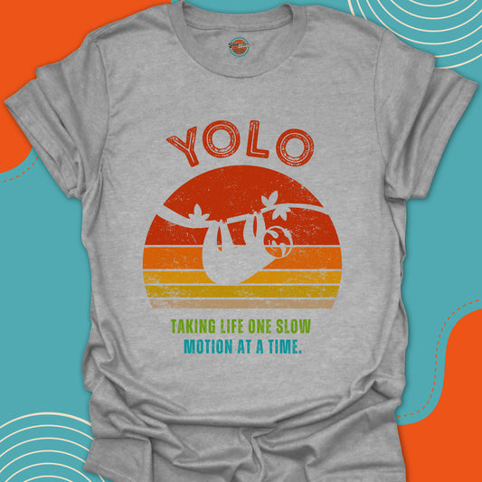 Gray t-shirt with 'YOLO' graphic and a sloth in silhouette against a sunset and text on a colorful background