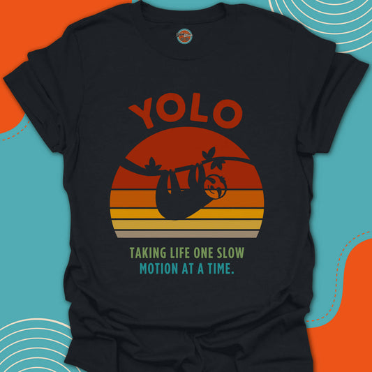 Black t-shirt with 'YOLO taking life one slow motion at a time' text and smiling sloth graphic on a round sunset background